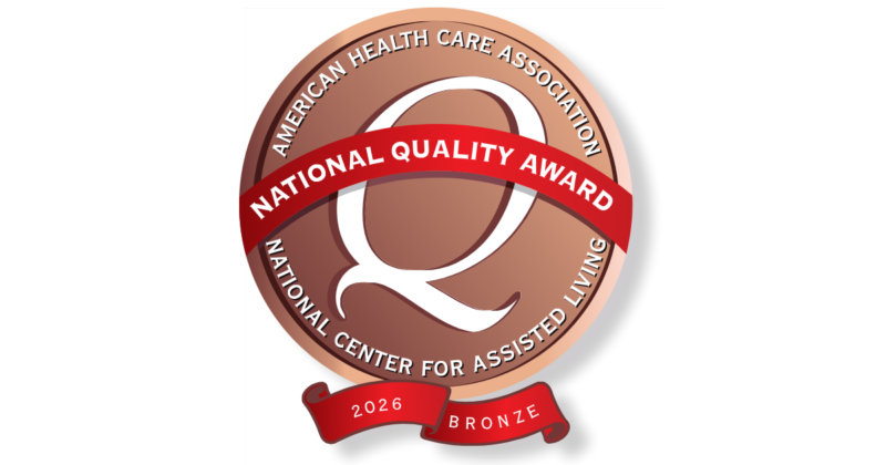 A circular bronze-colored badge with a red ribbon across the center reading 
