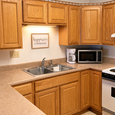 A kitchen with wooden cabinets, a double sink, a microwave, a coffee maker, a stove, and a decorative sign that reads 