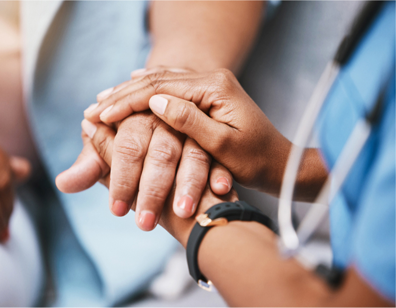 Close-up of two people holding hands, one with darker skin and the other with lighter skin; the person with darker skin is wearing a smartwatch and a stethoscope.